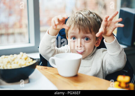 Ritratto di carino adorabile bambino caucasico kid boy bere il latte dalla tazza bianca di mangiare la prima colazione il pranzo la mattina presto, lo stile di vita quotidiana momenti sinceri Foto Stock