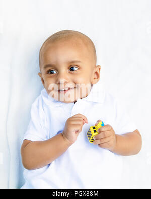 Ritratto di carino adorabile sorridente ridere little indian razza mista infant boy in maglia bianca su sfondo bianco giocando con auto giocattolo Foto Stock