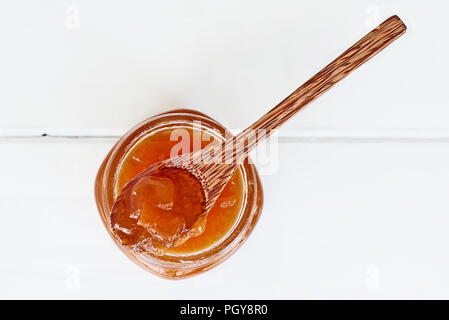 Scatto dall'alto di un cucchiaio di legno pieno di fatti in casa di melone marmellata di riposo in un vaso aperto riempito con la marmellata. Profondità di campo con il fuoco selettivo Foto Stock