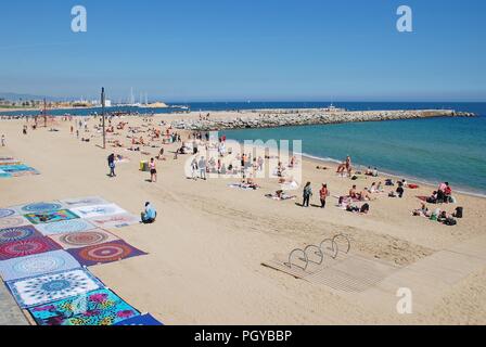 Le persone che si godono la spiaggia di Barcellona in Catalogna, Spagna il 17 aprile 2018. Un commerciante vende coperte in primo piano. Foto Stock