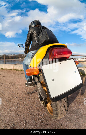 Posteriore, un ampio angolo di visione in bianco chiaro targa del moto, il pilota seduto sulla moto gialla Foto Stock