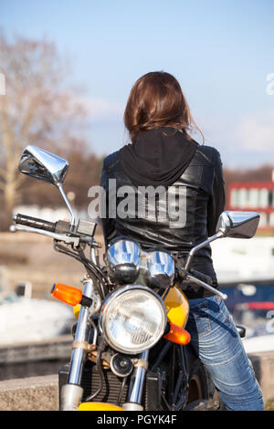 La donna caucasica in black leather jacket girare indietro su mentre è seduto sul motociclo Foto Stock