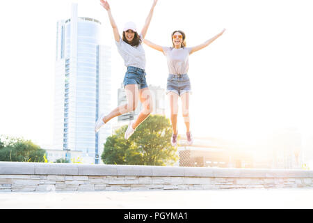 Due giovani felici hipster ragazze divertendosi, sorridente, ridere, jumping, passeggiate all'aperto sulla strada, estate rilassatevi concept Foto Stock