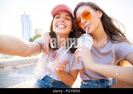 Due giovani sorridenti ragazze divertirsi seduti su uno skateboard e prendendo un selfie presso il parco. Foto Stock