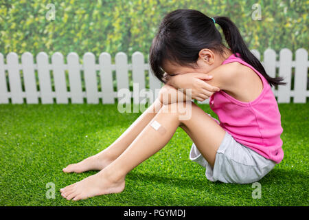 Asian Little Chinese ragazza seduta sul prato e a piangere al parco all'aperto Foto Stock