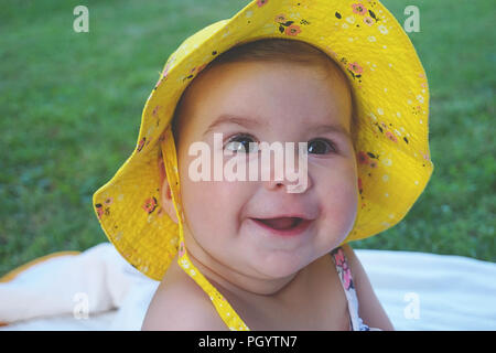 Ritratto di carino e felice bellissima bambina con cappello giallo sorridente e guardando in alto sul prato verde Foto Stock