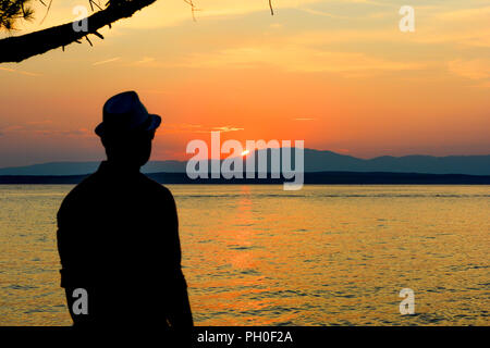 Silhouette di un uomo presso il bellissimo tramonto sulla spiaggia. Sfondo. Giovane uomo guardando il tramonto Foto Stock