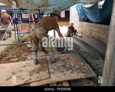 CHUUK, Stati Federati di Micronesia (Giugno 14th, 2018) Builder 3° di classe Jessica Maciejewski, assegnato alla Naval Mobile Battaglione di costruzione (NMCB) 11, Costruzione azione civica dettaglio Stati Federati di Micronesia, utilizza un rastrello per spostarsi attorno in calcestruzzo per accertarsi che non vi siano di bassa o alta spot. NMCB-11 è distribuito per eseguire la costruzione, umanitari e di assistenza estera, il teatro e la cooperazione in materia di sicurezza nel VII flotta area di operazioni. Foto Stock