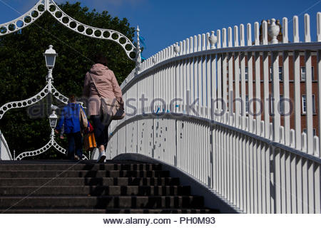 Una donna attraversa il Hal'penny Bridge a Dublino come il sole caldo bagna il centro citta'. La previsione è per temperature di 17 gradi e miscelati peri Foto Stock