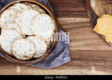 Scatto dall'alto di una tazza di acqua di cracker e fette di formaggio cheddar oltre un rustico sfondo. Copia gratuita dello spazio disponibile. Foto Stock