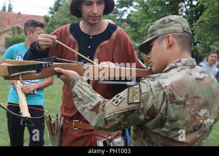 GRAČANICA, Kosovo - i soldati da multinazionali Battle Group- Oriente ha trascorso la giornata gustando la terza edizione del Festival Internazionale del borgo medievale di arti e mestieri-SHIELD, nel cortile del re Milutin Scuola Elementare di Gračanica, Kosovo, il 23 giugno. Pfc. Israele A. Reynero con Apache truppa, 3° Stormo, 61o reggimento di cavalleria, seconda della brigata di fanteria combattere la squadra, 4a divisione di fanteria, crossbow riceve istruzioni da un locale master Gračanica a bracci. Foto Stock