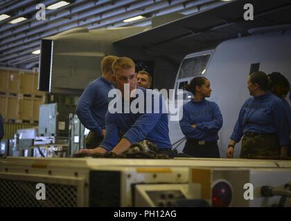 5TH FLOTTA AREA DI OPERAZIONI (26 giugno 2018) Airman Simon Schultz, da Stevens Point, Wisconsin, aziona un come32-32spotting un dolly in hangar bay di wasp-classe assalto anfibio nave USS Iwo Jima (LHD 7), 26 giugno 2018. Iwo Jima, homeported a Mayport Fla., è sulla distribuzione per gli Stati Uniti Quinta Flotta area di operazioni a sostegno della sicurezza marittima operazioni per rassicurare gli alleati e partner e preservare la libertà di navigazione e il libero flusso di commercio nella regione. Foto Stock