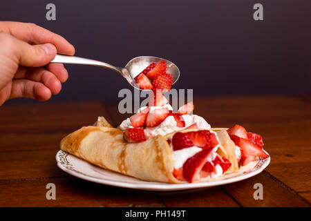 Golden crepes con fragole e panna montata con le fragole essendo spooned on-top. Foto Stock