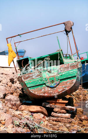 Vecchia barca da pesca. La vecchia barca da pesca bloccati sulla costa rocciosa in Egitto. Abbandonata in legno barca da pesca di variopinti colori isolati sulla spiaggia. Foto Stock