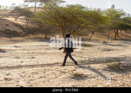 Deserto LAMPOUL, SENEGAL - Apr 23, 2017: Non identificato uomo senegalesi indossa il cofano e camminate lungo la strada in un deserto Lampoul, bellissimo paesaggio luogo Foto Stock