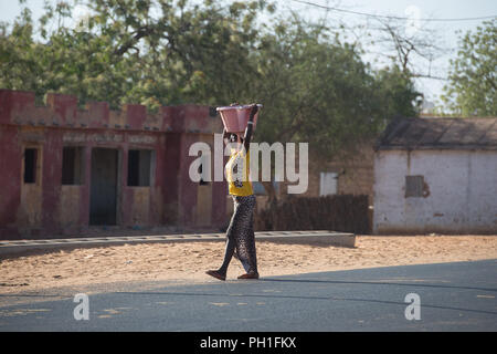Deserto LAMPOUL, SENEGAL - Apr 23, 2017: Non identificato donna senegalese trasporta un bacino sul suo capo lungo la strada in un villaggio vicino al deserto Lampoul Foto Stock