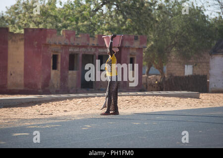Deserto LAMPOUL, SENEGAL - Apr 23, 2017: Non identificato donna senegalese trasporta un bacino sul suo capo lungo la strada in un villaggio vicino al deserto Lampoul Foto Stock