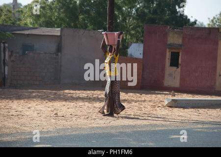 Deserto LAMPOUL, SENEGAL - Apr 23, 2017: Non identificato donna senegalese trasporta un bacino sul suo capo lungo la strada in un villaggio vicino al deserto Lampoul Foto Stock