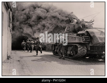 WW2 GI soldati del 55th corazzato battaglione di fanteria Terza Armata e M4 Sherman serbatoio del serbatoio xxii battaglione, passate si muovono attraverso il fumo riempita street. Wernberg, Germania. Aprile 22, 1945 Foto Stock