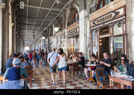 Persone a pranzo tavoli fuori in ombra sotto il porticato al Caffè Florian e Piazza San Marco, San Marco, Venezia, Veneto, Italia durante la European hea Foto Stock