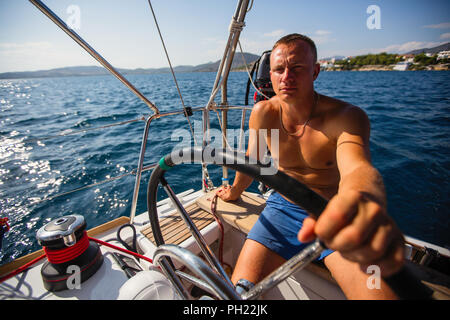 L'uomo corre skipper di una barca a vela in mare aperto. Foto Stock