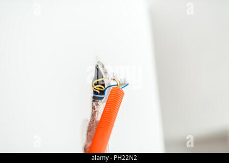 Nuovo cablaggio elettrico installazione con fili da una presa e la giunzione in una parete entrando in una sezione di arancio brillante condotto. Foto Stock