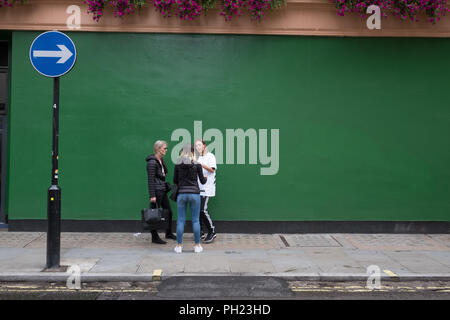 Parete Verde e una freccia plus i passanti in una strada di Londra a Soho, Londra Foto Stock