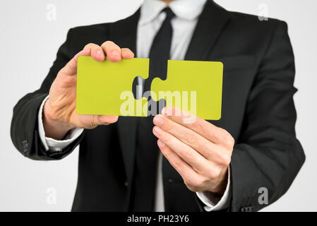 Imprenditore in un vestito con due pezzi di un puzzle giallo concettuale del problem solving, pianificazione, creatività, lo sviluppo e la sfida, close up v Foto Stock