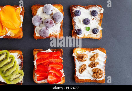 French Toast con formaggio a pasta morbida, fragole, kiwi, noci e mirtilli su una scheda di colore nero, vista dall'alto Foto Stock