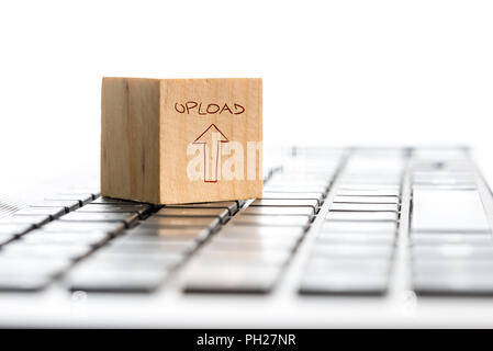 Computer caricare il concetto con un cubo di legno con una mano-freccia disegnata e word - Upload - su un bianco della tastiera del computer isolato su bianco con copyspace. Foto Stock