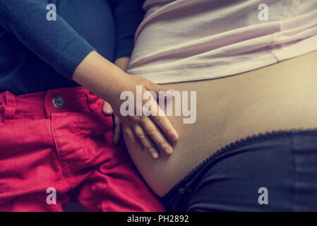 Retrò l immagine del bambino trattenendo il suo madri incinte di incollaggio del ventre con il nascituro in una mostra di amore, closeup dei womans di stomaco e la mano di Foto Stock