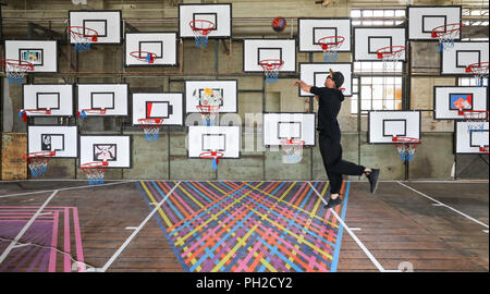 Germania a Leipzig. 24 Ago, 2018. Curatore Denis Leo Hegic getta una palla da basket in l'installazione 'giocando con opere d'Arte". 97 cesti da basket su pareti a traliccio, sfere e i pavimenti sono parte dell'opera d'arte, che in realtà è solo creato dai visitatori giocando lungo durante la mostra. L'Arte Urbana Festival 'Monumenta' si apre il 1 settembre nella fabbrica di vuoto sale dell'ex Pittlerwerke. Il Monumenta presenta graffiti, arte di strada e arte contemporanea su circa 6 mila metri quadrati fino al 13 Ottobre. Credito: Jan Woitas/dpa-Zentralbild/dpa/Alamy Live News Foto Stock