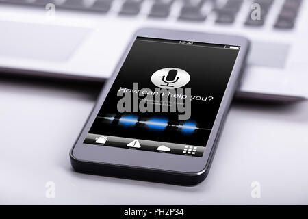 Smart Phone sulla scrivania con schermo che mostra in che modo posso aiutarla? Testo Foto Stock
