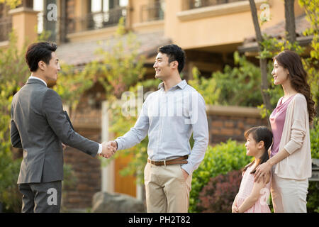 Felice famiglia giovane stringono le mani con agente immobiliare Foto Stock