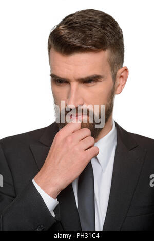 Imprenditore in pensieri profondi tocca la sua barba con una mano e guarda verso il basso con una seria faccia. Professional catturato al suo lavoro. Foto Stock