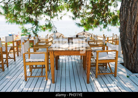 Ristorante con tavoli su un bianco di neve, terrazza che si affaccia sul mare sotto rami di pino. Foto Stock