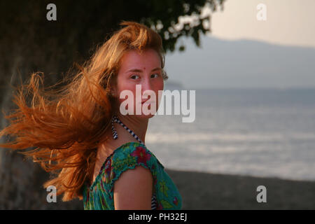 Un giovane, lo zenzero donna di fronte a un lago Foto Stock