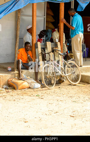 Strada di BISSAU GUINEA B. - 1 Maggio 2017: Non identificato gli uomini locali sedersi vicino al magazzino in un villaggio in Guinea Bissau. Ancora molte persone nel paese liv Foto Stock