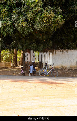 Strada di BISSAU GUINEA B. - 1 Maggio 2017: Non identificato gli uomini locali sedetevi accanto alla strada in un villaggio in Guinea Bissau. Ancora molte persone nel paese li Foto Stock