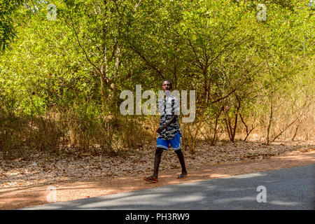 Strada di BISSAU GUINEA B. - 1 Maggio 2017: locale non identificato uomo cammina accanto alla strada in un villaggio in Guinea Bissau. Ancora molte persone nel paese Foto Stock