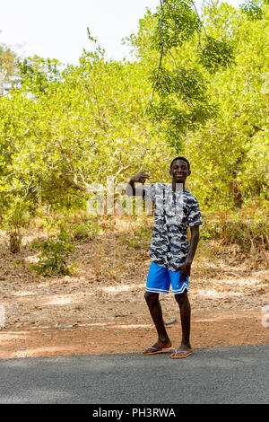 Strada di BISSAU GUINEA B. - 1 Maggio 2017: Non identificato uomo locale sorge di fianco alla strada e sorrisi in un villaggio in Guinea Bissau. Ancora molte persone in Foto Stock