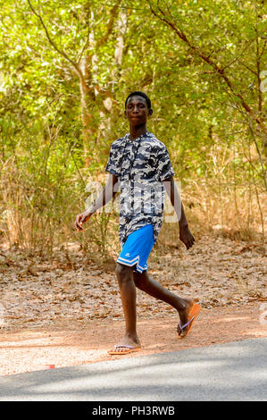 Strada di BISSAU GUINEA B. - 1 Maggio 2017: locale non identificato uomo cammina accanto alla strada in un villaggio in Guinea Bissau. Ancora molte persone nel paese Foto Stock