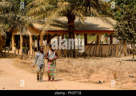Strada di BISSAU GUINEA B. - 1 Maggio 2017: locale non identificato l uomo e la donna a piedi lungo la strada in un villaggio in Guinea Bissau. Ancora molte persone in Foto Stock
