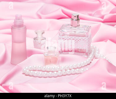 Bottiglie di profumo con corda di perle bianche sul rosa tessuto di seta Foto Stock