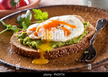 Una fetta di pane tostato con deliziosa avocado, uova fritte e salsa piccante. Foto Stock