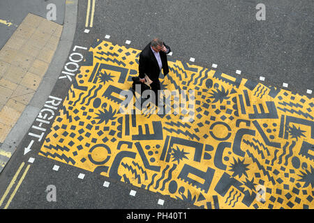 Kishimoto illustrazione geometrica e imprenditore a piedi con valigetta ventiquattrore su giallo attraversamento pedonale vicino Aldersgate nella città di Londra UK KATHY DEWITT Foto Stock