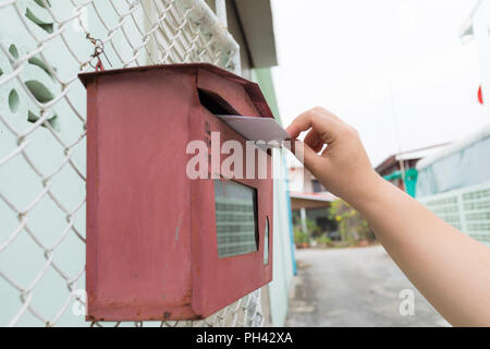 Inviare una lettera a Red britannico postbox sulla strada, Primo piano su una donna di mano come ella è la pubblicazione di una lettera, Foto Stock