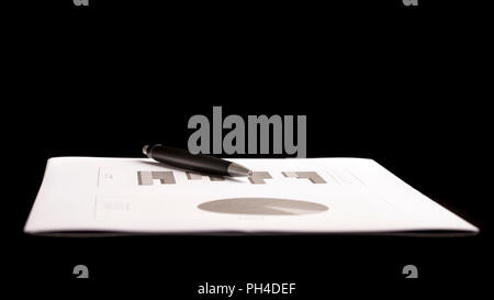 Penna concettuale sulla parte superiore del documento aziendale con grafici isolati su sfondo nero, sottolineando la copia dello spazio. Foto Stock