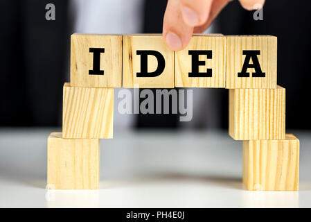 Il concetto ispiratore di una persona per costruire un ponte di legno con cubetti di idea di parola scritta su di essi Foto Stock