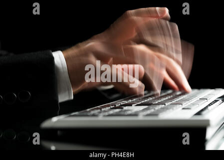Vista dettagliata del maschio sfocate mani digitando sulla tastiera del computer. Su sfondo nero. Foto Stock
